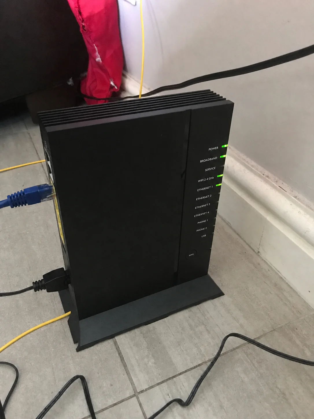 Black broadband router with connected cables and front indicator lights.
