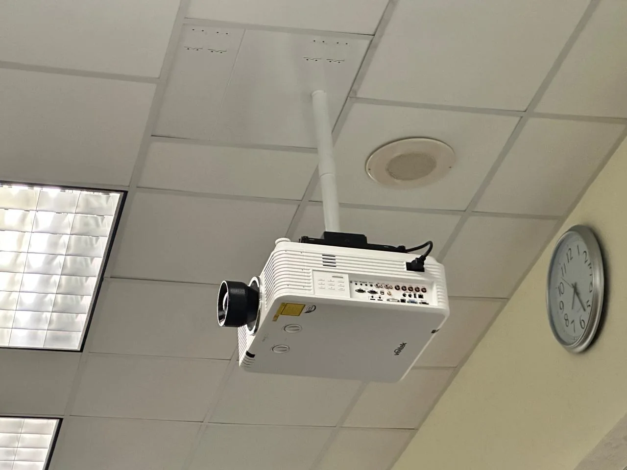 White projector suspended from a ceiling mount with connected cables and nearby ceiling speaker.