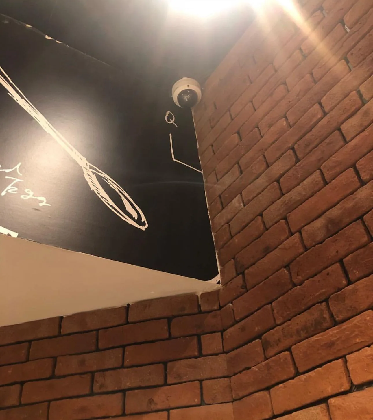Dome surveillance camera mounted near a ceiling above a brick wall with visible cable routing.