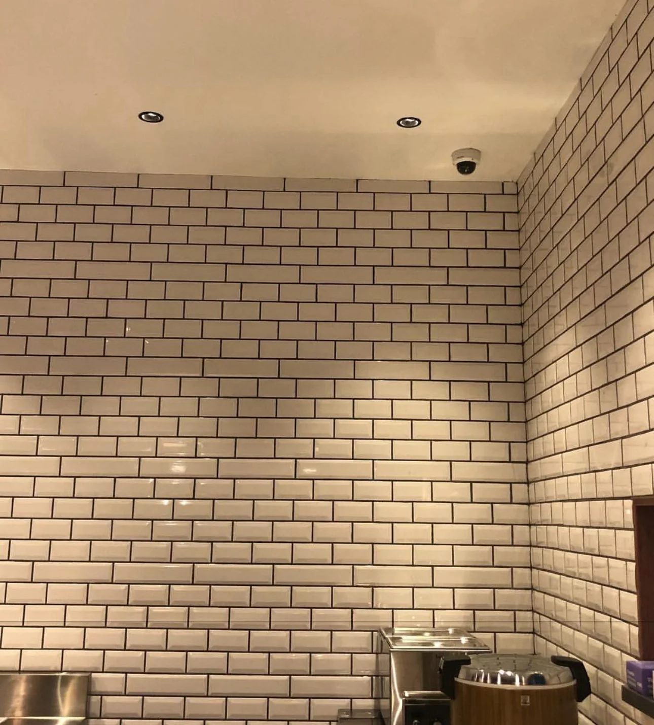 Dome camera installed near recessed ceiling lights above tiled walls in an interior room.