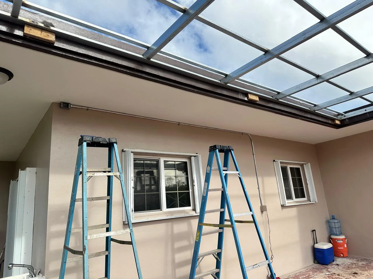 Exterior building wall beneath a canopy with ladders and conduit routed above windows and doors.