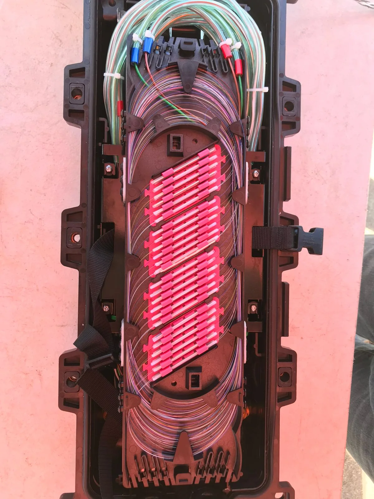 Open fiber splice closure with organized fibers and red protective sleeve holders.