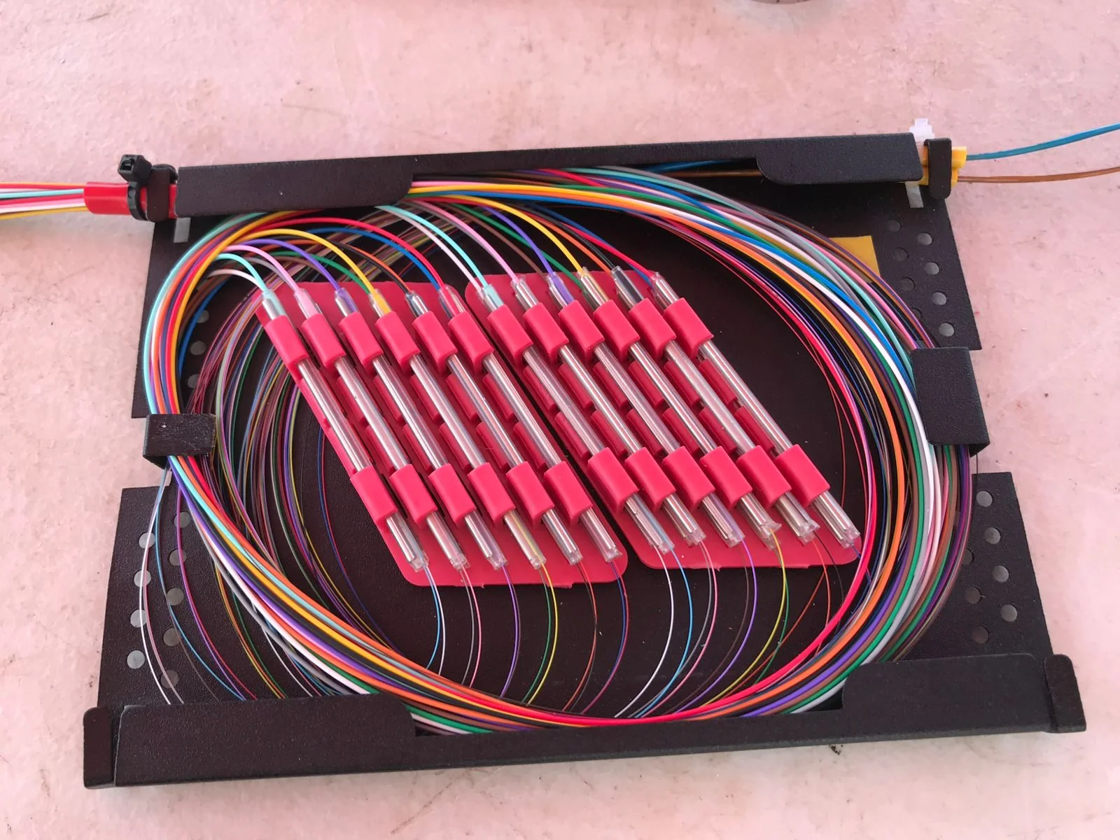 Compact black splice tray containing color-coded fibers and red splice protectors.