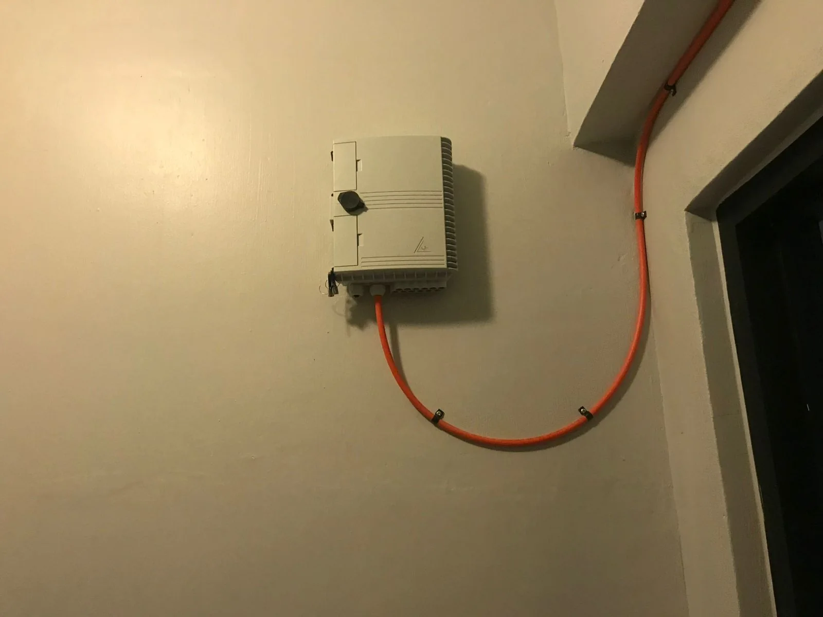 Wall-mounted fiber termination box connected to orange protective conduit.