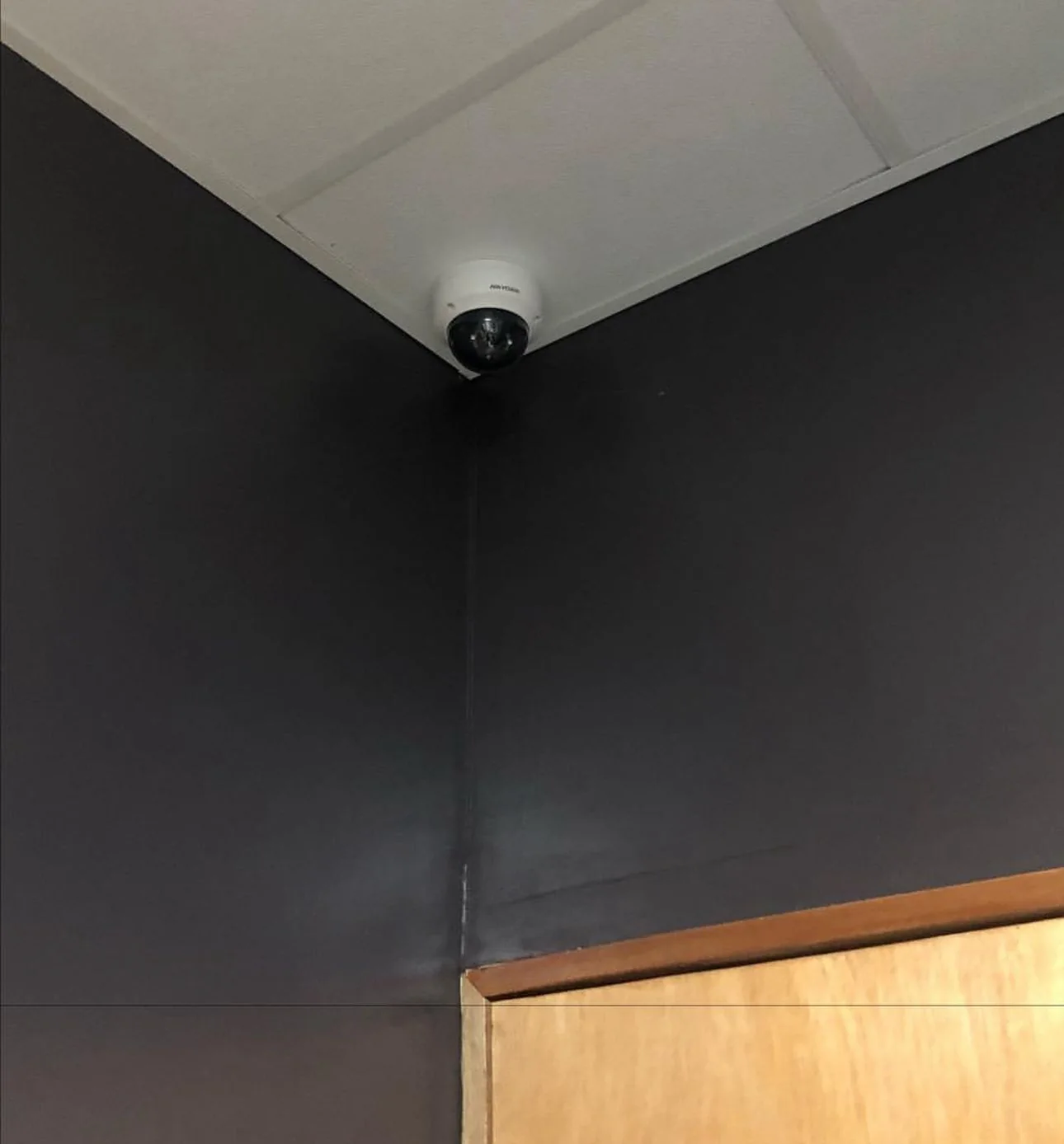 White dome surveillance camera installed at the ceiling corner above an interior doorway.