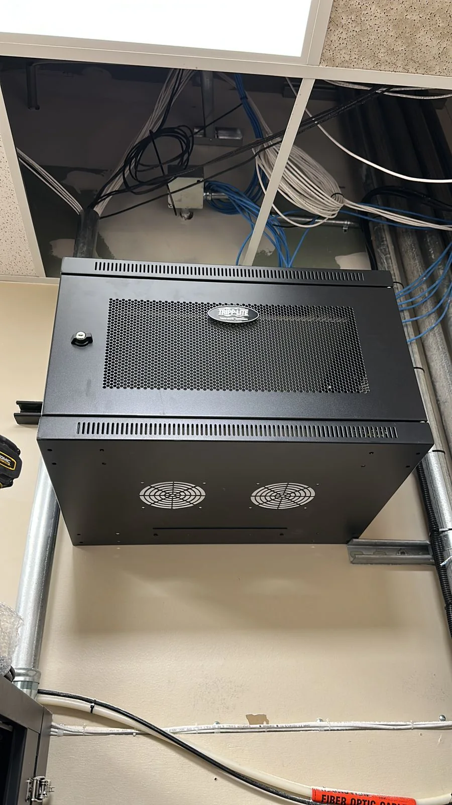 Wall-mounted network cabinet with cabling routed above the ceiling.
