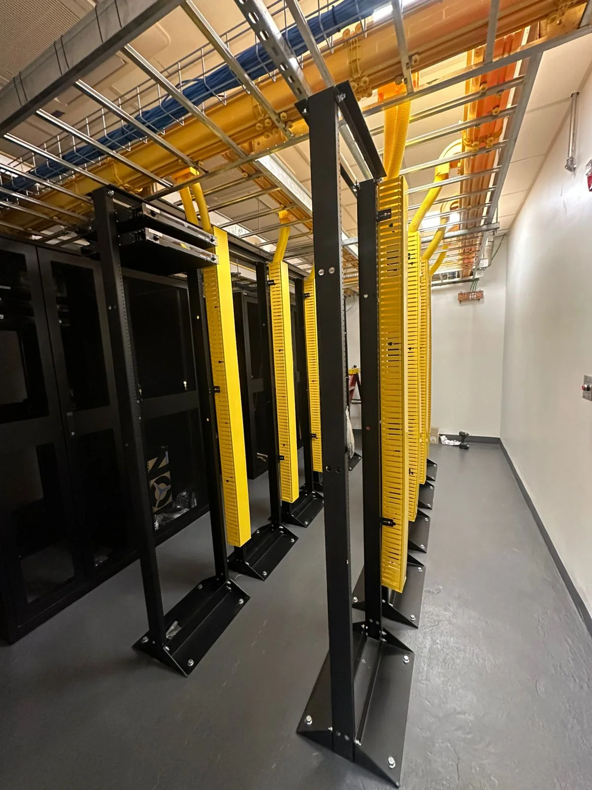 Network racks beneath overhead cable trays and yellow fiber-routing channels.