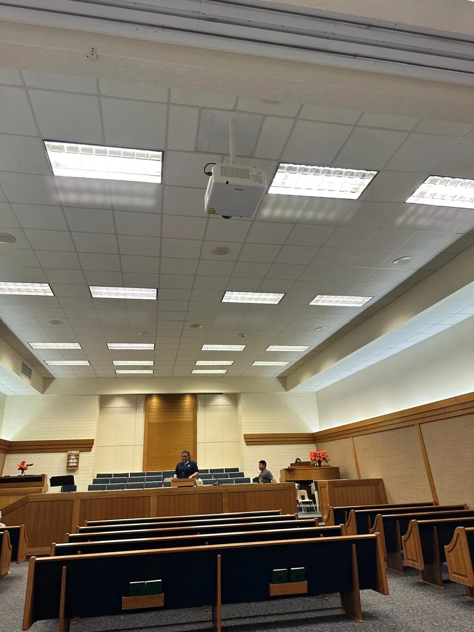 Ceiling-mounted projector above rows of seating in an indoor presentation space.