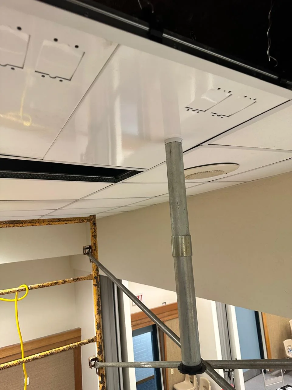 Projector mounting pole and cable pathway beneath an opened suspended ceiling panel.