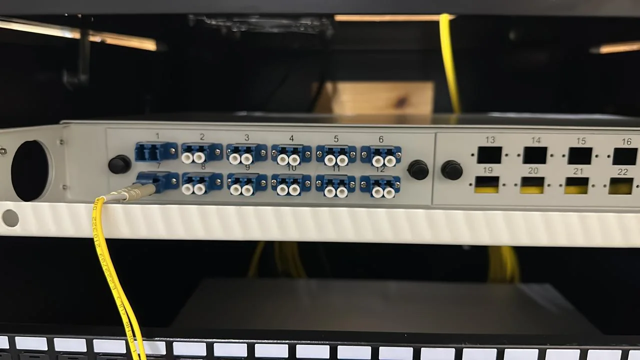 Rack-mounted fiber patch panel with blue adapters and a connected yellow fiber patch cable.
