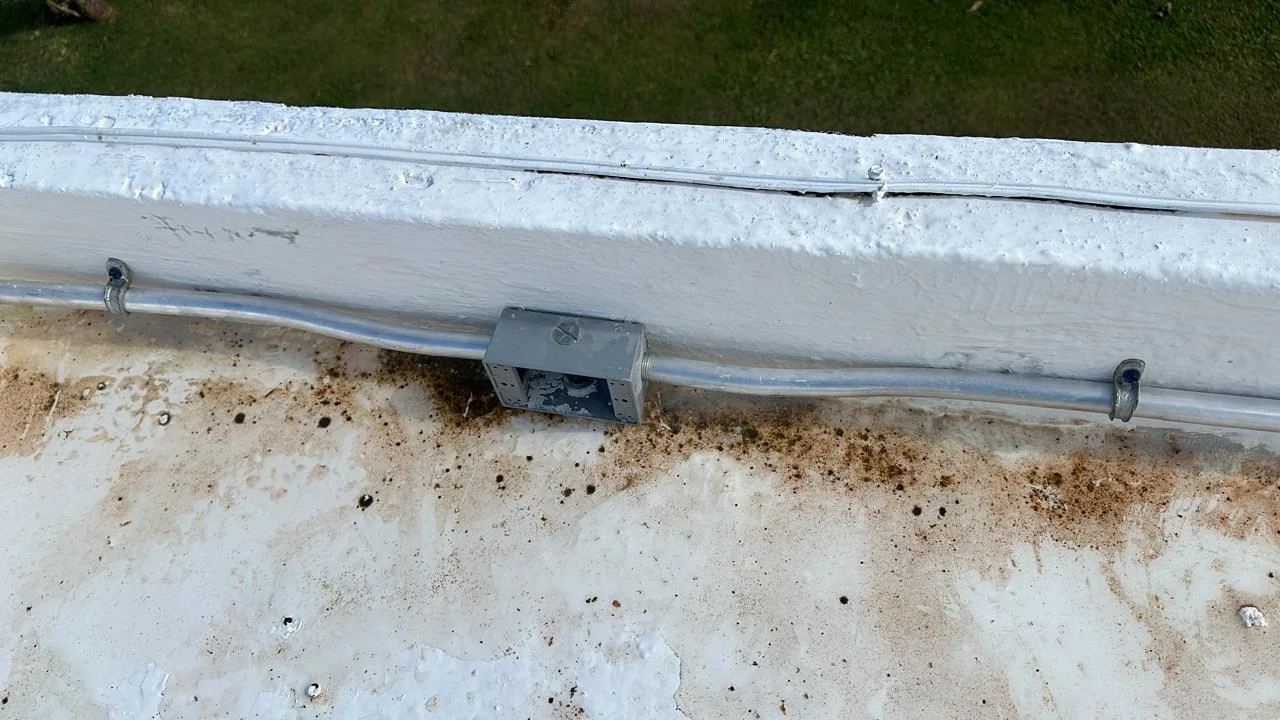 Close view of metal conduit, fixings, and a junction box installed along a roof parapet.