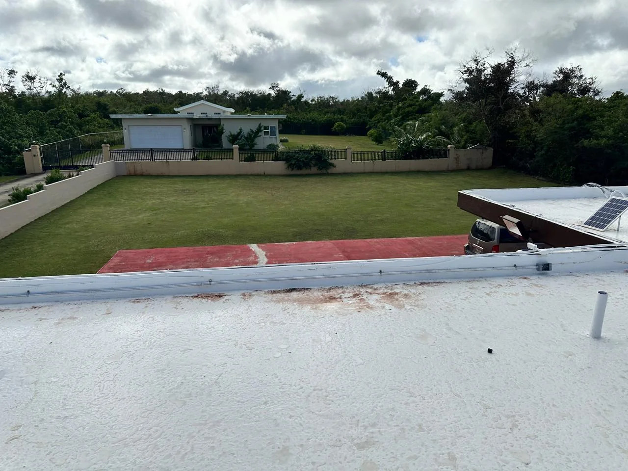 Metal conduit and junction boxes following a roof parapet with a residential yard beyond.