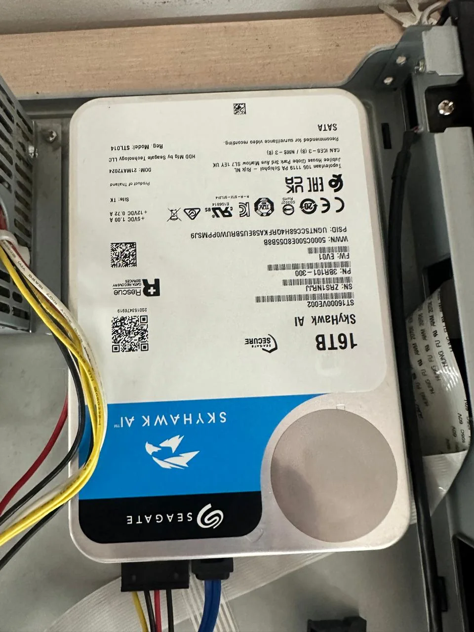 Storage hard drive mounted inside an open surveillance recorder beside its power and data connections.