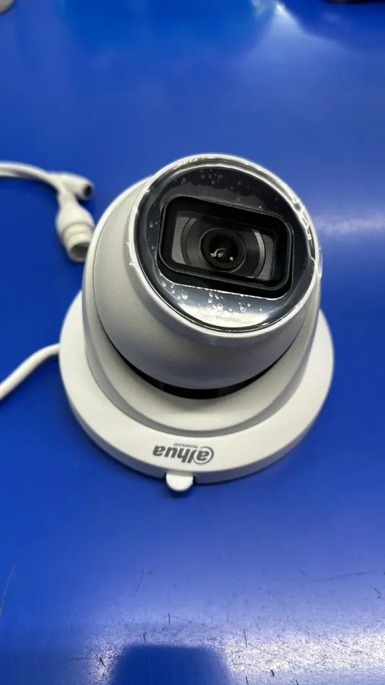 White turret surveillance camera with a black lens housing resting on a blue work surface.