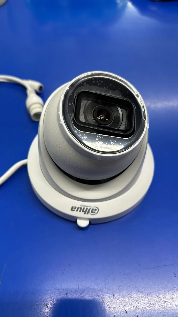 White turret surveillance camera with a black lens housing resting on a blue work surface.