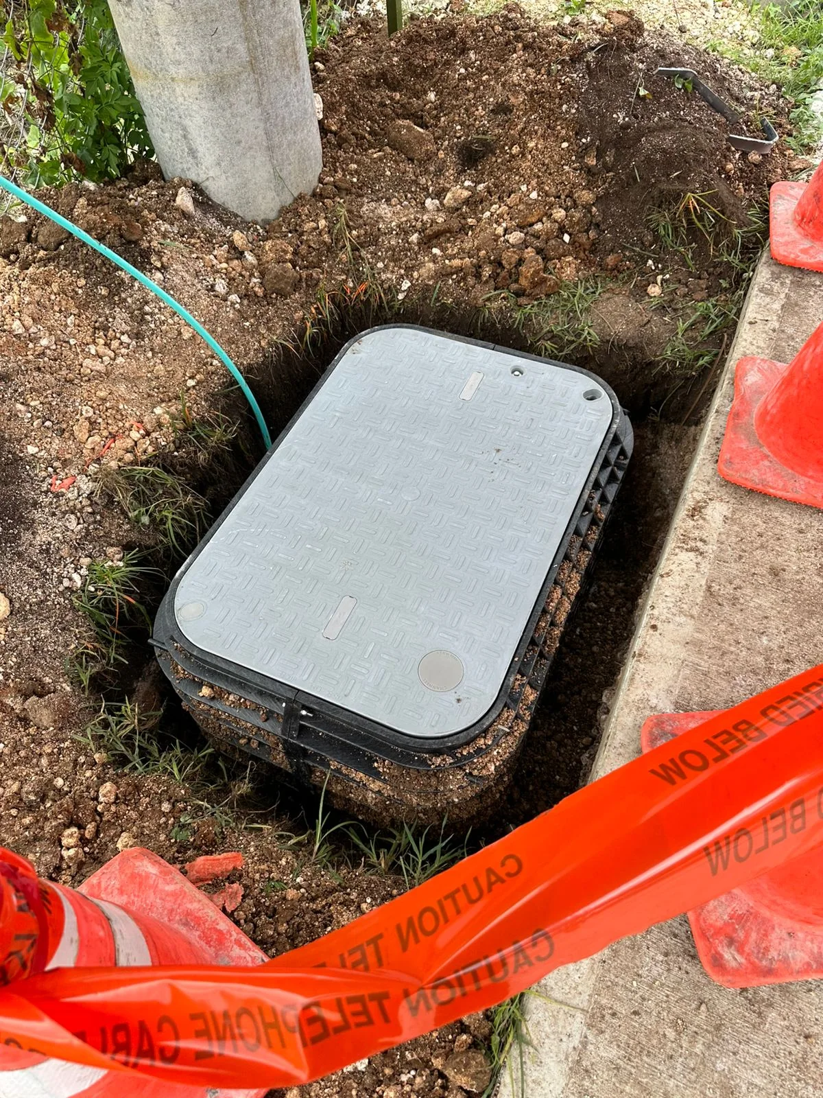 Underground handhole set into an excavated area beside a concrete sidewalk.