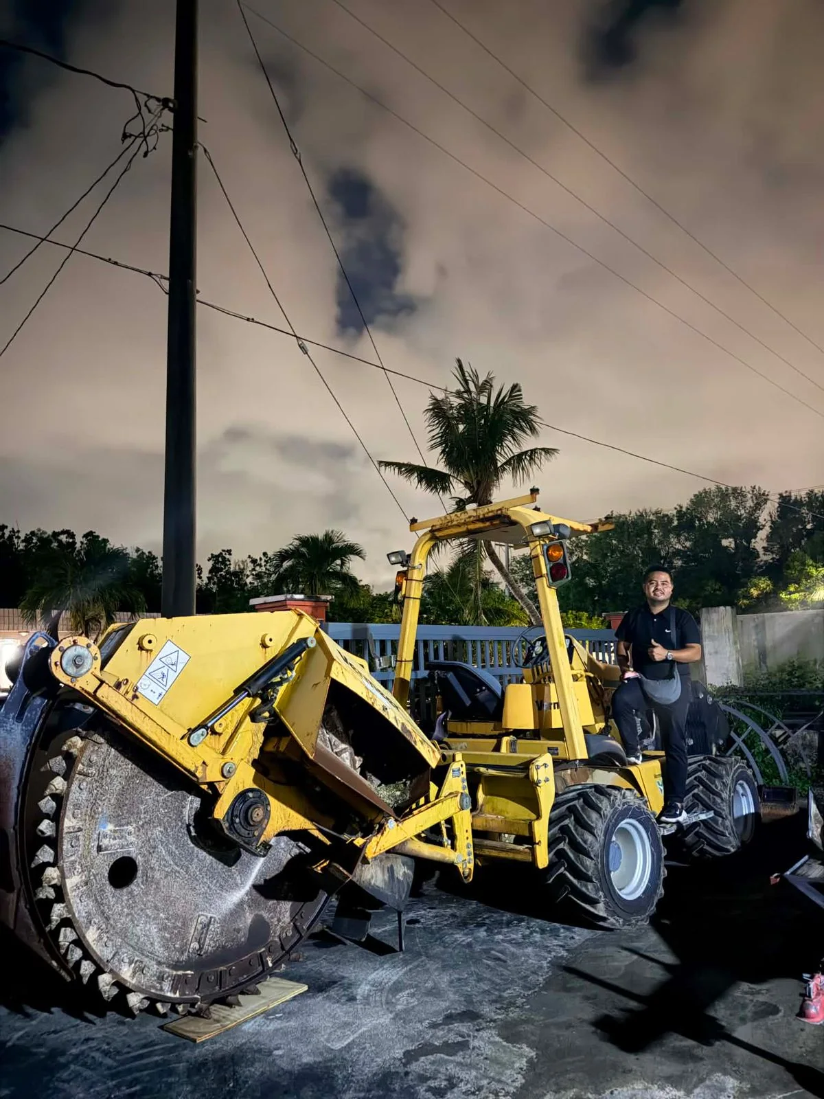 Person standing beside a yellow wheel trencher photographed at night.