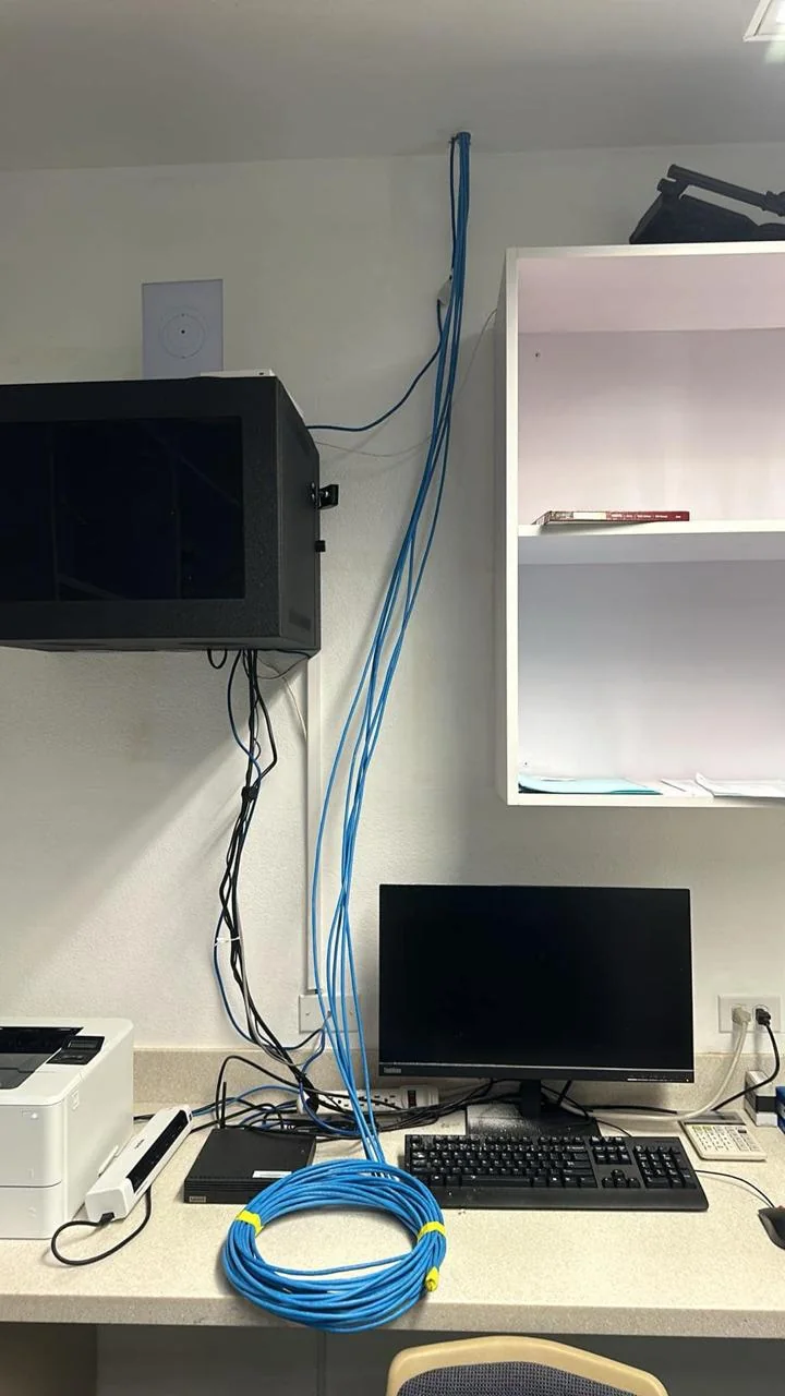 Computer workstation beneath a wall-mounted display with blue cables routed along the wall.