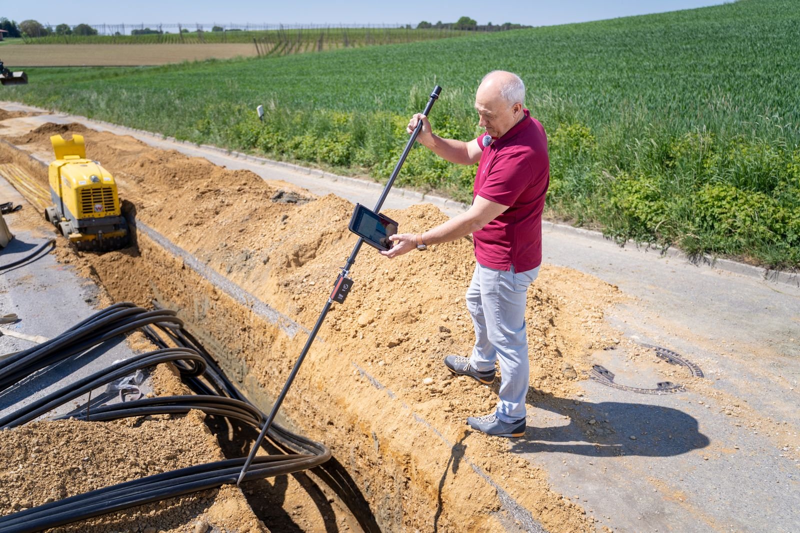 Engineer using surveying equipment beside an exposed underground cable route.
