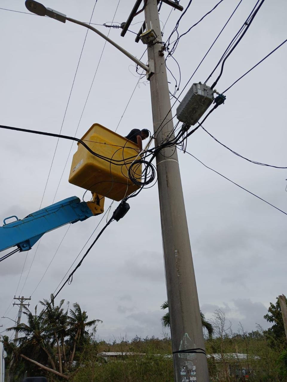Technician working from an elevated bucket near telecommunications cabling.